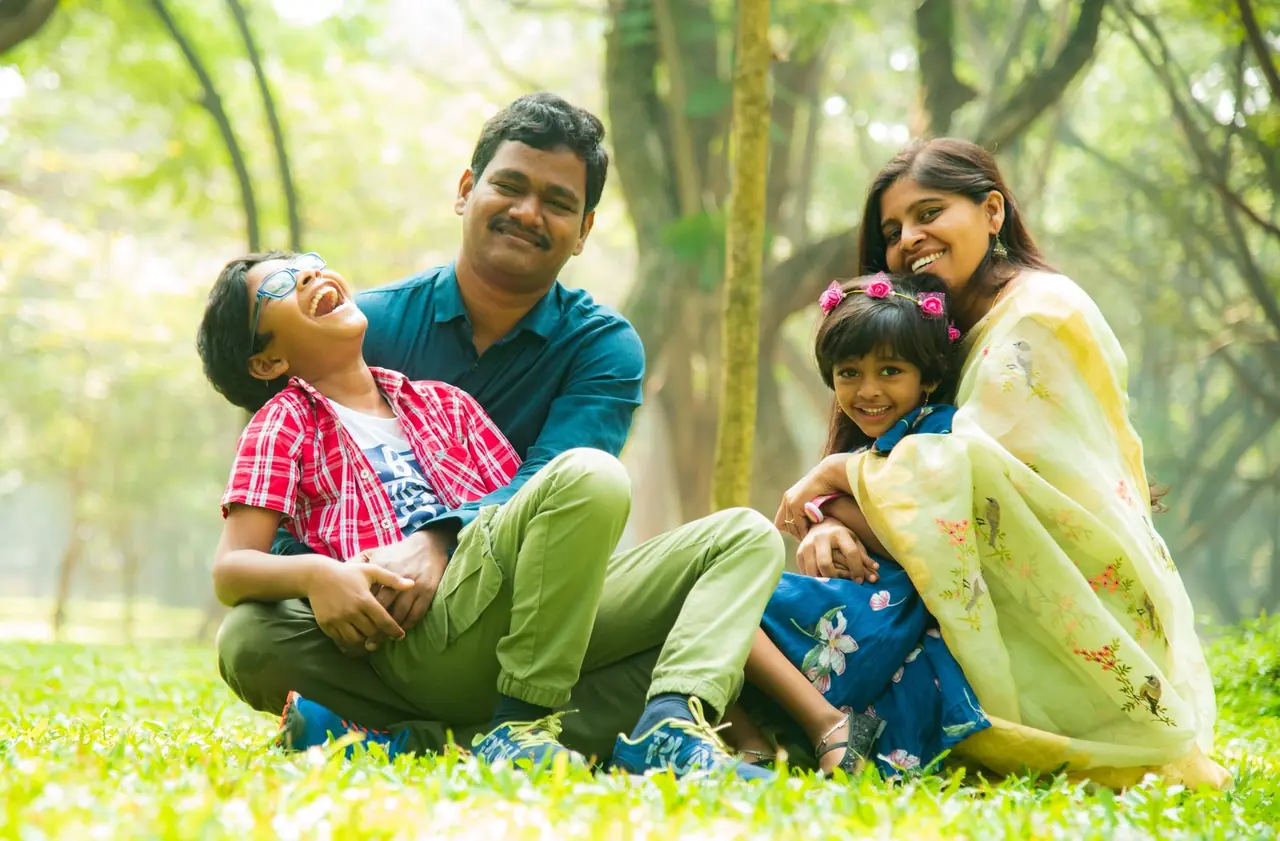 Cheerful Indian family sitting together on the grass in a park — everything you care about, protected within reach